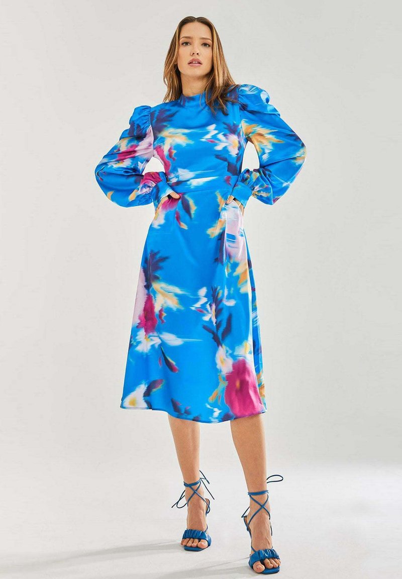 Blue floral midi dress with puff sleeves, featuring pink and yellow patterns. Paired with blue strappy heeled sandals. Smooth fabric texture.