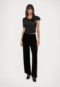 Crni crop top s jednim rukavom i cvjetnim detaljem. Crne baršunaste hlače širokog kroja, uparene s crnim cipelama na visoku petu. Glatka tekstura.