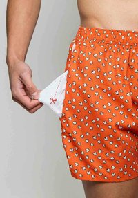 Boxeurs en coton orange avec un motif de popcorn, comprenant une poche blanche avec un design de ciseaux rouges. Ceinture élastique visible.