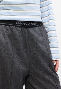 Sorte bukser med texturet overflade og elastisk talje, der viser "NØRGAARD" i grå. Sammen med en lyseblå stribet langærmet skjorte.