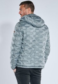 Light gray puffer jacket with a hood, featuring a quilted design and smooth texture. Includes a side patch detail on the sleeve.