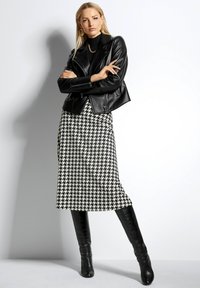 Schwarze Leder-Motorradjacke über einem schwarzen Rollkragenpullover, kombiniert mit einem schwarz-weißen Hahnentritt-Midikleid und kniehohen schwarzen Stiefeln.