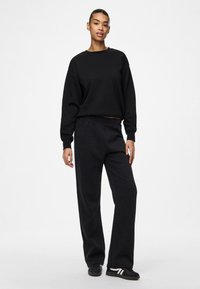 Zwarte oversized sweater en losse sweatpants van katoen, voorzien van geribbelde boorden en tailleband, gecombineerd met zwarte schoenen.