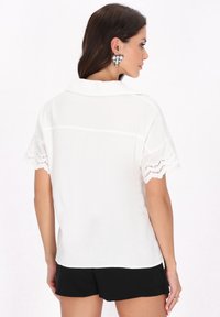 Weiße kurzärmlige Bluse mit strukturierter Oberfläche und gewellter Spitzenborte an den Ärmeln, versehen mit einem klassischen Kragen und lockerer Passform.