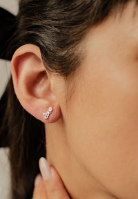 Pendientes de plata en forma de la palabra "amor", con una superficie lisa y pulida, montados en un lóbulo de oreja de tono de piel.