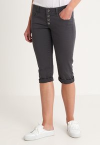 Pantalons cropped gris en mélange de coton, avec une fermeture à boutons, deux poches avant et des manches retroussées. Associés à des chaussures blanches à enfiler.