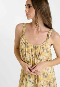 Mouwloze, vloeiende jurk in geel met een aquarel-effect; heeft een geraffineerde halslijn en dunne banden; zachte textuur, lichtgewicht stof.