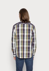 Camicia a maniche lunghe a quadri nei colori blu, verde, giallo e bianco. Presenta polsini con bottoni e un orlo curvo. Tessuto di cotone con motivo a scacchi.