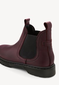 Botín Chelsea de cuero burdeos con paneles laterales elásticos, costuras decorativas y suela de goma texturizada. Tirador en la parte trasera para ponérselo fácilmente.