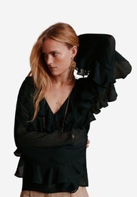 Zwarte ruffle blouse met een diepe V-hals, lange transparante mouwen en een gelaagd volants ontwerp. Lichtgewicht stof met een vloeiende textuur.