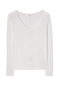 Bijela košulja dugih rukava s okruglim izrezom, lagane tkanine i vidljivim detaljima šavova na ovratniku i rubu.