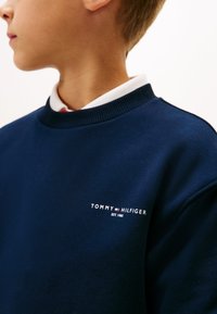 Felpa blu navy in cotone con scollatura rotonda e polsini a costine. Presenta un logo bianco: "TOMMY HILFIGER EST. 1985" sul petto.