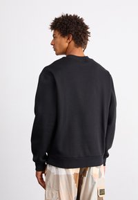 Hanorac negru cu guler rotund și mansete ribbed, având o croială lejeră. Purtați-l cu pantaloni scurți bej cu model, prezentând un design simplu pe spate.