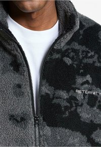 Giacca in pile grigia e nera con motivo camouflage, dotata di colletto alto, chiusura con zip e logo "RETERNITY" in argento.