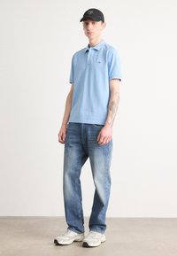 Lyseblå polo t-skjorte med korte ermer, brukt med lyseblå denimjeans. Grå og hvite sneakers, svart caps med logo. Enkelt og uformelt utseende.
