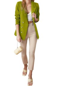 Limonkowo-zielona marynarka dwurzędowa, biały krótki top, beżowe spodnie na miarę, kremowa torba typu bucket oraz jasne sandały. Gładkie faktury i elegancki design.