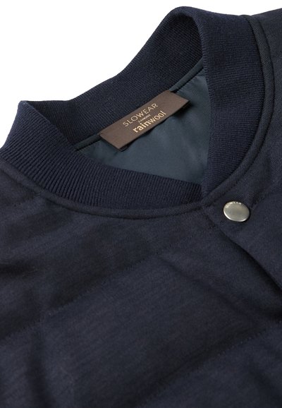 Marineblauer Wollcardigan mit geripptem Kragen, einem einzelnen metallischen Druckknopf und einem glatten Innenfutter mit einem Markenetikett.