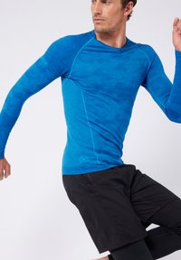 Maglietta sportiva a maniche lunghe in un blu vivace con una finitura testurizzata, caratterizzata da cuciture a contrasto, abbinata a pantaloni corti sportivi neri.