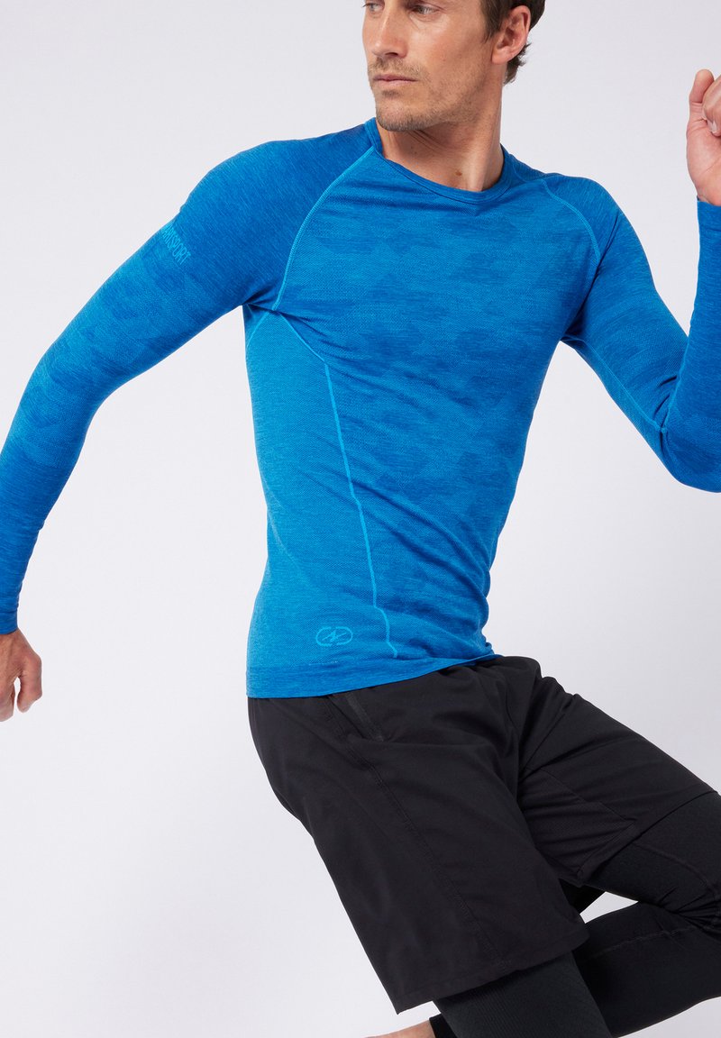 Maglietta sportiva a maniche lunghe in un blu vivace con una finitura testurizzata, caratterizzata da cuciture a contrasto, abbinata a pantaloni corti sportivi neri.