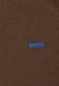 Tissu de pull en tricot marron avec une surface texturée et une étiquette rectangulaire bleue avec un texte en relief.