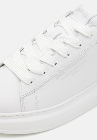 Hvit lær sneakers med tykk gummisåle, rund tå og flate hvite lisser. Har preget logo på siden og sømdetaljer.