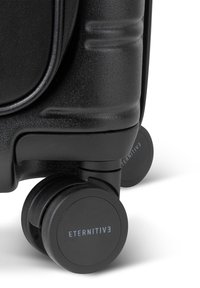 Schwarzer Koffer mit strukturierter Oberfläche, robustem Design, vier 360-Grad-Rädern und blauer "ETERNITIV3"-Markierung auf dem Rad.