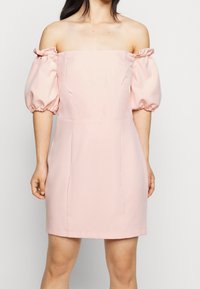 Růžové šaty bez ramínek s nabíranými rukávy, přiléhavým tělem a délkou nad kolena. Hladká tkanina s minimem švů a čistými liniemi.