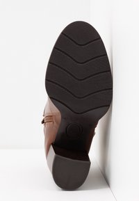 Hnědá kožená bota s texturovanou černou gumovou podrážkou se vzorem cikcak. Boční zip a minimalistické designové detaily.