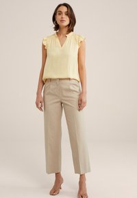 Blusa gialla a riflessi con scollo a V, abbinata a pantaloni beige a gamba larga. Tessuto morbido, vestibilità rilassata. Design semplice, senza motivi.