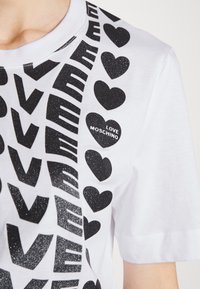 Wit T-shirt met zwarte glinsterende tekst "LOVE" en hartvormen, één hart draagt de tekst "LOVE MOSCHINO" op de borst.