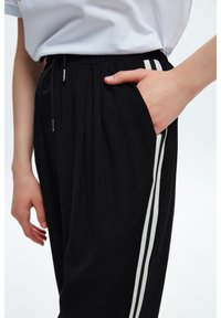 Svarta träningsbyxor i mjukt tyg med två vita sidostripes, resår i midjan och en sidoficka.