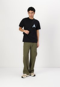 Black cotton t-shirt with graphic print, olive green cargo pants featuring side pockets, and beige sneakers with black accents.