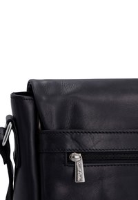 Černá kožená crossbody taška s překlopným víkem, vybavená přední zipovou kapsou a stříbrnými kovovými detaily. Hladký povrch, minimalistický design.