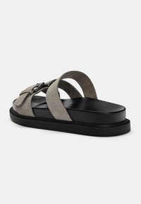 Sandali in suede grigi con doppie cinghie incrociate, una base nera imbottita e un leggero plateau. Presenta un dettaglio decorativo a fibbia sulla cinghia.