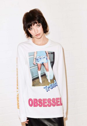 Long-sleeve white t-shirt featuring a large graphic print of a person in a trendy outfit, with colorful text "Trendy" and "OBSESSED."