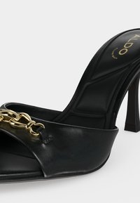 Mule noire à talon haut avec semelle intérieure rembourrée, bout ouvert, détail chaîne dorée sur la bride avant et logo ALDO sur la semelle intérieure.