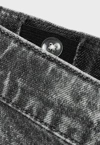 Tela de mezclilla gris con una superficie ligeramente texturada, que presenta un botón redondo y transparente en la parte superior, y detalles de costura en contraste.