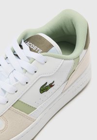 Hvite lær sneakers med grønne og beige detaljer. Har en teksturert tunge, runde snøring og brodert logo på siden.