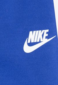 Zila dziju auduma ar gludu tekstūru, kurā ir izteikts balts Nike logotips un izliekta svītra.
