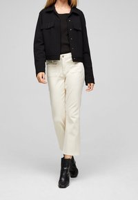 Svart kort jacka med knäppning fram, två bröstfickor, kombinerad med krämfärgade vida byxor och svarta ankelstövlar med ett texturerat mönster.