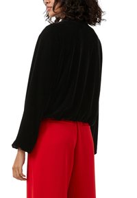 Zwart fluwelen top met lange mouwen en verzaagde onderzoom. Gecombineerd met high-waisted, op maat gemaakte rode broek. Glad oppervlak en relaxte pasvorm.