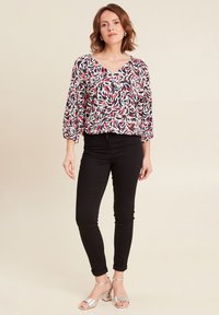 Blusa con motivo floreale, scollo a V, maniche puff a 3/4, nei colori rosso, blu navy e bianco, abbinata a jeans skinny neri e sandali con tacco argentati.