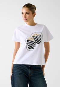 Wit katoenen T-shirt met een afbeelding van twee gestreepte popcornbakken met kettingen en pareldetails. Ronde halslijn en korte mouwen.