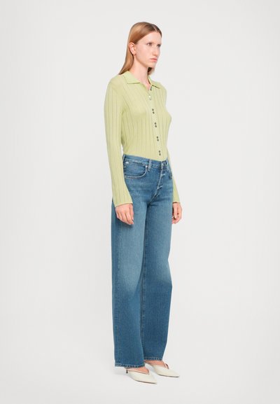 Light green ribbed knit long-sleeve shirt with buttons, paired with wide-leg blue jeans and white heels. Simple, fitted design with a collar.