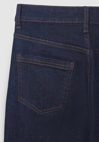 Jean denim bleu foncé avec des coutures orange visibles, présentant une seule poche arrière et une texture lisse. La ceinture est droite et bien définie.