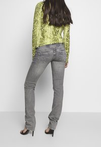 Formsynta grå denimjeans med klassisk skärning, i kombination med en långärmad topp i klart grön ormtryck. Höga svarta sandaler.