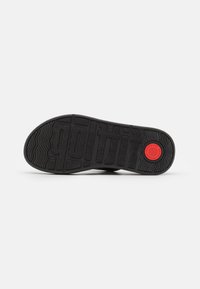 Sole della sneaker nera con scanalature testurizzate e un evidente motivo "gothit". Presenta un accento rosso circolare vicino al tallone.
