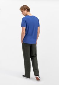 Blauwe T-shirt met korte mouwen en een ronde halslijn, gecombineerd met losse, donkergroene broek en zwarte sneakers, weergegeven vanaf de achterkant.