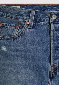 Jeans in denim blu con rivetti in rame, dettagli sfrangiati e cuciture a contrasto arancioni. Presentano un classico design a cinque tasche e passanti per cintura.