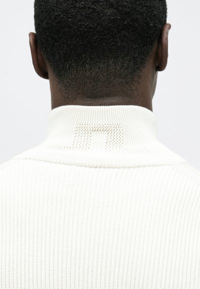 Col roulé blanc côtelé avec un col texturé présentant un accent subtil à motif au dos. Matière en maille douce, design minimaliste.